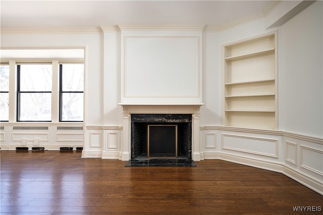 unfurnished living room with a premium fireplace, dark wood-type flooring, built in shelves, and ornamental molding