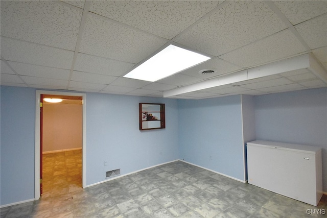 basement with a drop ceiling and refrigerator