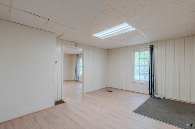 unfurnished room featuring a paneled ceiling, wooden walls, and light wood-type flooring