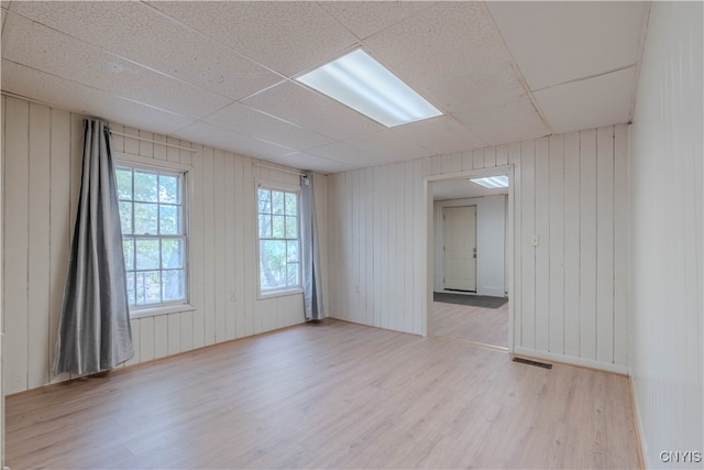 empty room featuring a drop ceiling, wooden walls, and light wood-type flooring