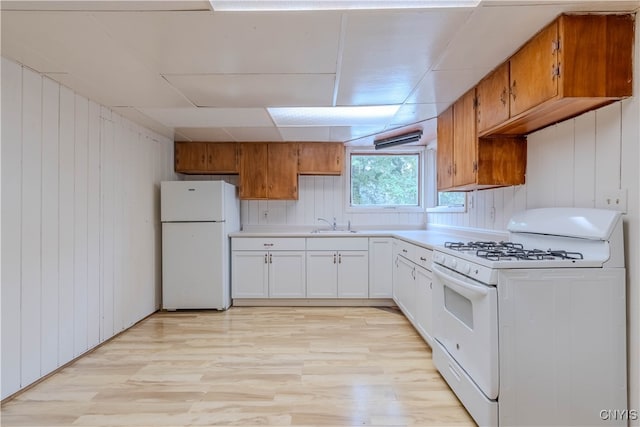 kitchen with light hardwood / wood-style floors, white cabinets, wooden walls, and white appliances