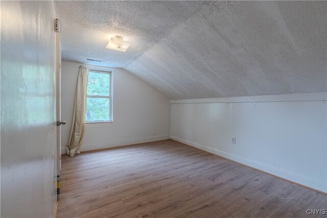 additional living space featuring a textured ceiling, lofted ceiling, and light hardwood / wood-style flooring