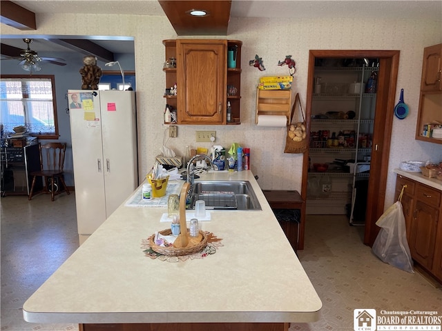 kitchen featuring sink, ceiling fan, beamed ceiling, white fridge, and a kitchen island with sink