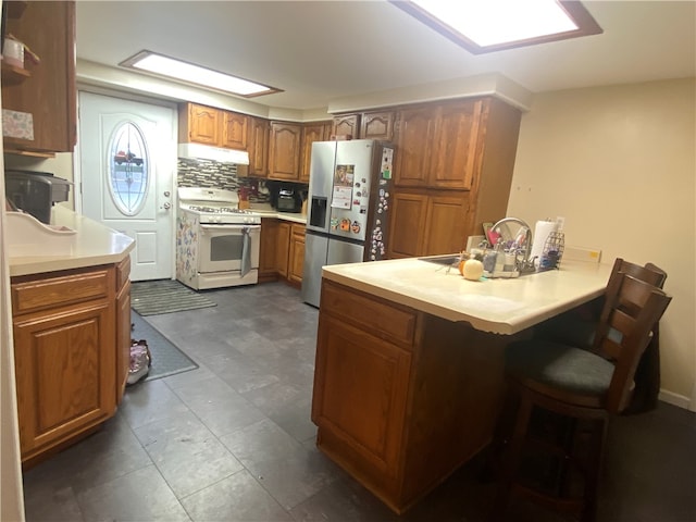 kitchen with kitchen peninsula, backsplash, gas range gas stove, stainless steel fridge, and a breakfast bar