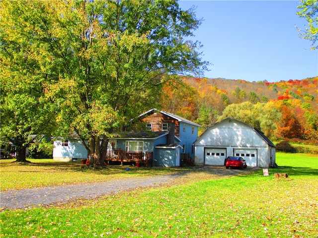 view of front of property featuring a wooden deck, a front yard, an outbuilding, and a garage