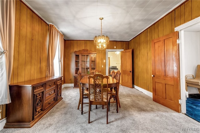 carpeted dining room with wooden walls, crown molding, and an inviting chandelier