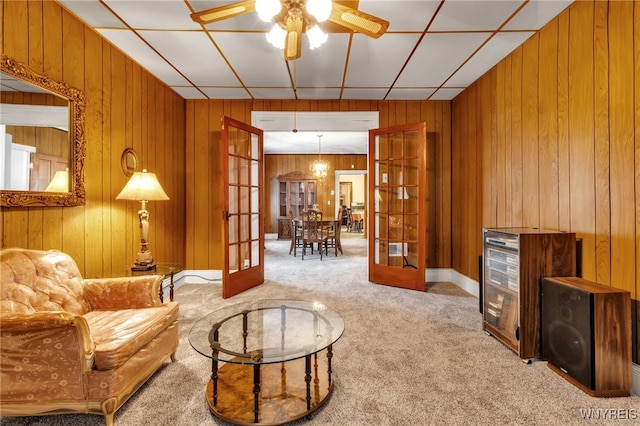 living area featuring french doors, light carpet, wooden walls, and ceiling fan