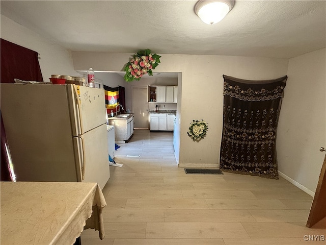 interior space with sink, white fridge, a textured ceiling, and light hardwood / wood-style floors