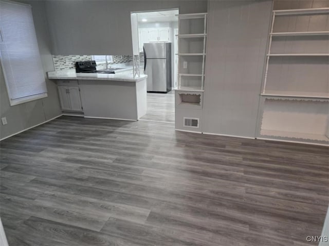 interior space featuring kitchen peninsula, decorative backsplash, stainless steel refrigerator, dark hardwood / wood-style floors, and black range with electric cooktop