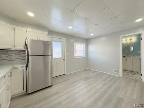 kitchen featuring white cabinetry, a drop ceiling, light wood-type flooring, stainless steel fridge, and backsplash