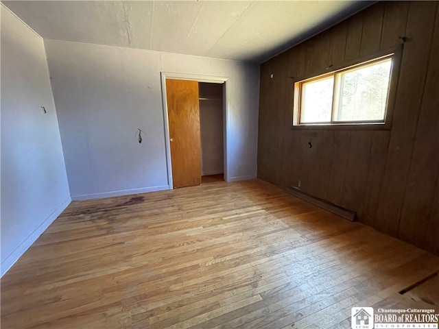 unfurnished room with a baseboard radiator, wooden walls, and light wood-type flooring