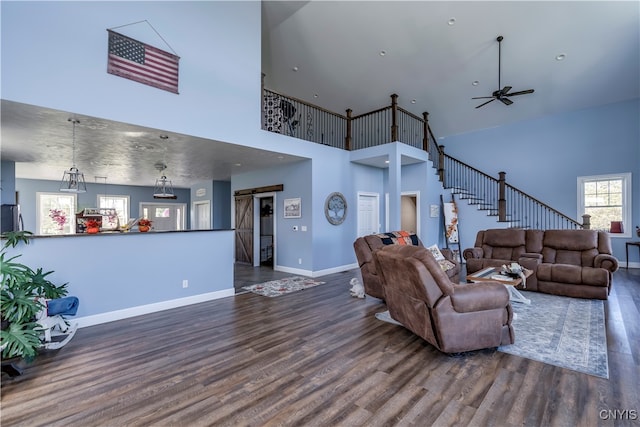 living room with a high ceiling, a barn door, dark wood-type flooring, and ceiling fan