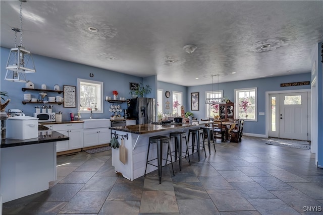 kitchen with a kitchen island, stainless steel fridge with ice dispenser, a kitchen bar, pendant lighting, and white cabinets