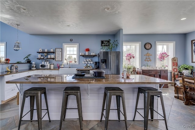 kitchen featuring stainless steel fridge, a kitchen breakfast bar, white cabinetry, sink, and a center island