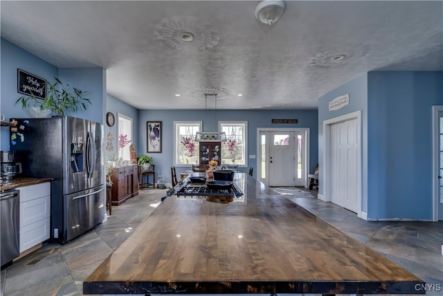 interior space with butcher block counters, stainless steel appliances, pendant lighting, white cabinetry, and a textured ceiling