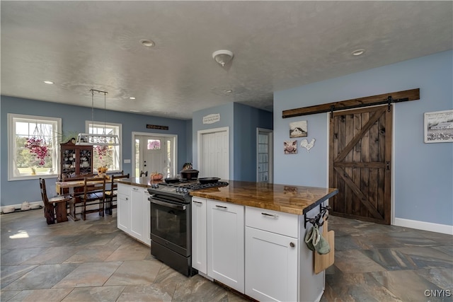 kitchen featuring gas stove, decorative light fixtures, a barn door, and white cabinets