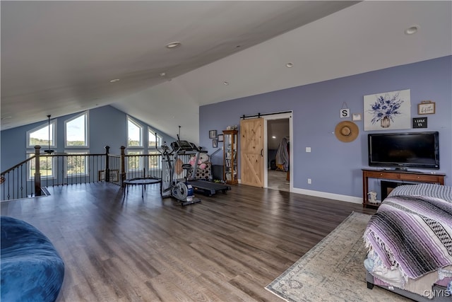 exercise room with a barn door, wood-type flooring, and vaulted ceiling