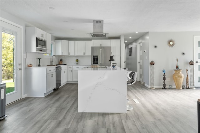 kitchen featuring light stone countertops, appliances with stainless steel finishes, a kitchen island, white cabinets, and light hardwood / wood-style flooring