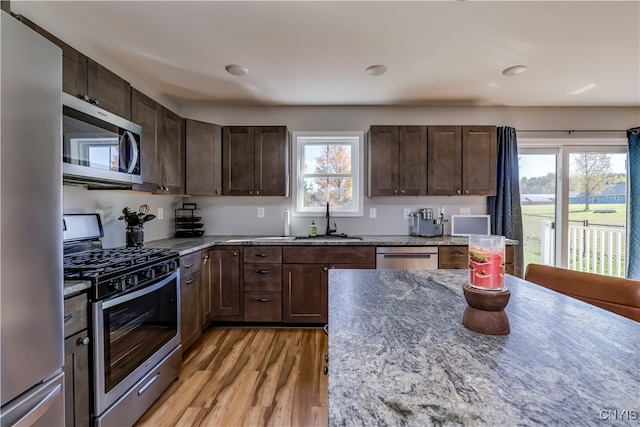 kitchen with light hardwood / wood-style flooring, stainless steel appliances, dark brown cabinets, sink, and light stone counters