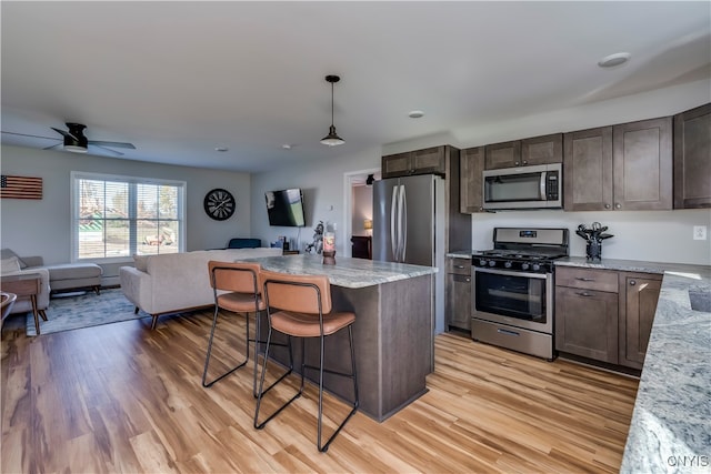 kitchen featuring hanging light fixtures, appliances with stainless steel finishes, a kitchen breakfast bar, light wood-type flooring, and light stone counters