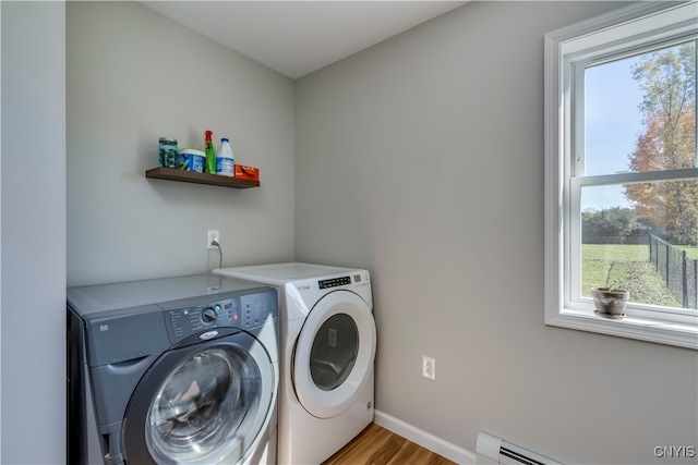 laundry area with a wealth of natural light, a baseboard heating unit, washing machine and dryer, and light hardwood / wood-style floors