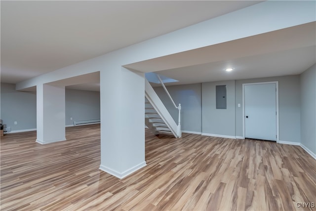 basement featuring a baseboard radiator, electric panel, and light wood-type flooring