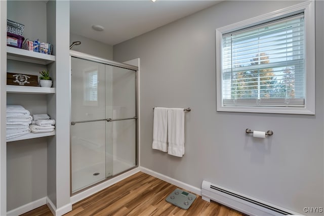 bathroom with a shower with door, a baseboard heating unit, and wood-type flooring