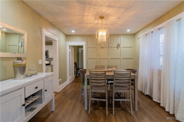 dining area with dark wood-type flooring, a textured ceiling, and an inviting chandelier