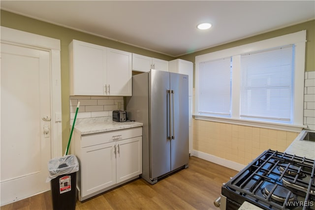 kitchen featuring black gas stove, light hardwood / wood-style flooring, high quality fridge, and white cabinets