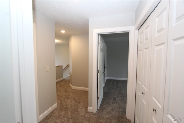 hallway with dark carpet and a textured ceiling