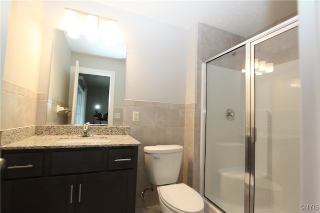 bathroom with toilet, vanity, tile walls, and a shower with door