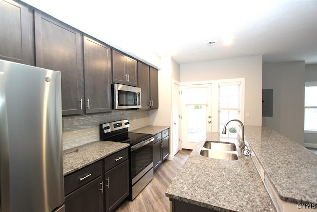 kitchen featuring appliances with stainless steel finishes, sink, an island with sink, dark brown cabinets, and light hardwood / wood-style floors