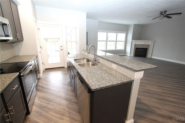 kitchen with appliances with stainless steel finishes, dark brown cabinets, sink, and a center island with sink