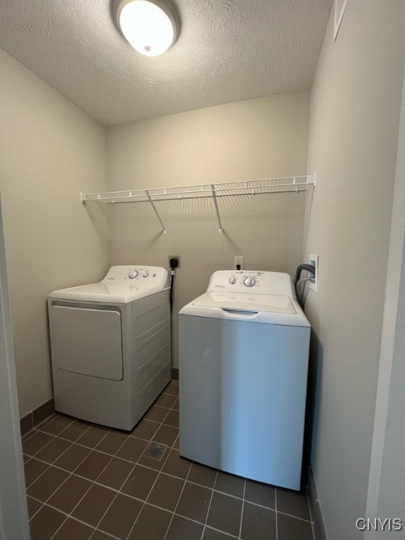 laundry room featuring a textured ceiling, washing machine and clothes dryer, and dark tile patterned flooring