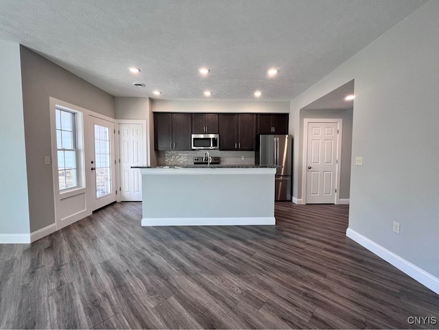 kitchen with dark brown cabinets, appliances with stainless steel finishes, dark hardwood / wood-style floors, and a kitchen island with sink