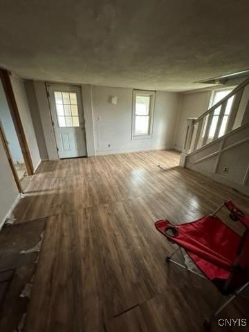 unfurnished living room with stairway, wood finished floors, and plenty of natural light