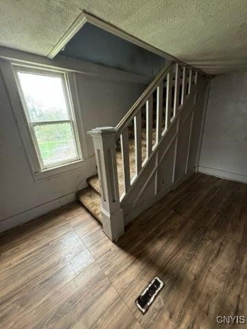 staircase with wood finished floors, a textured ceiling, and visible vents