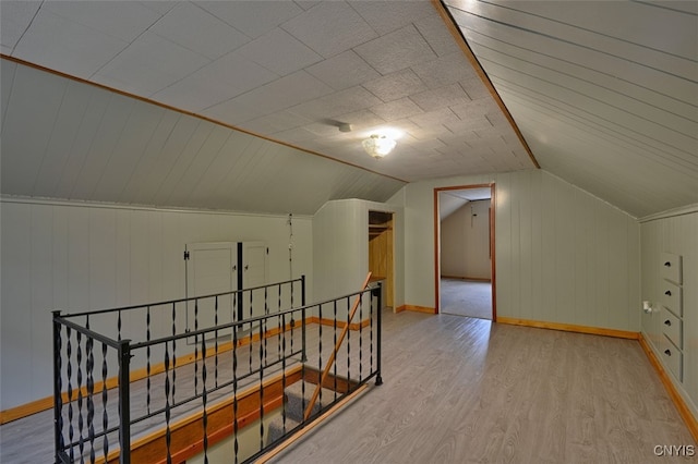 additional living space featuring vaulted ceiling, light hardwood / wood-style flooring, and wooden walls