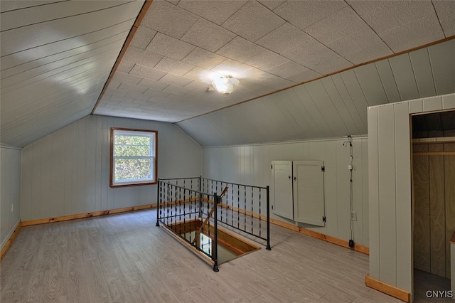 bonus room featuring lofted ceiling, wooden walls, and light wood-type flooring