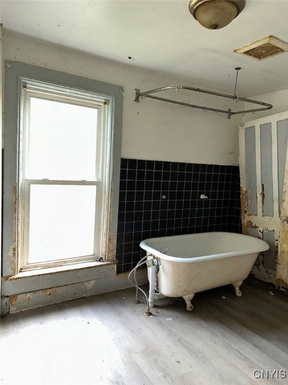 bathroom with hardwood / wood-style floors, tile walls, and a bath