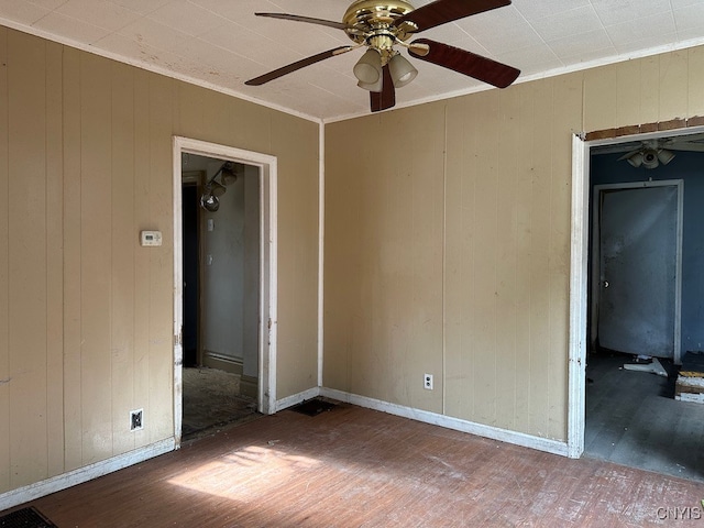 empty room with ornamental molding, wood walls, hardwood / wood-style floors, and ceiling fan