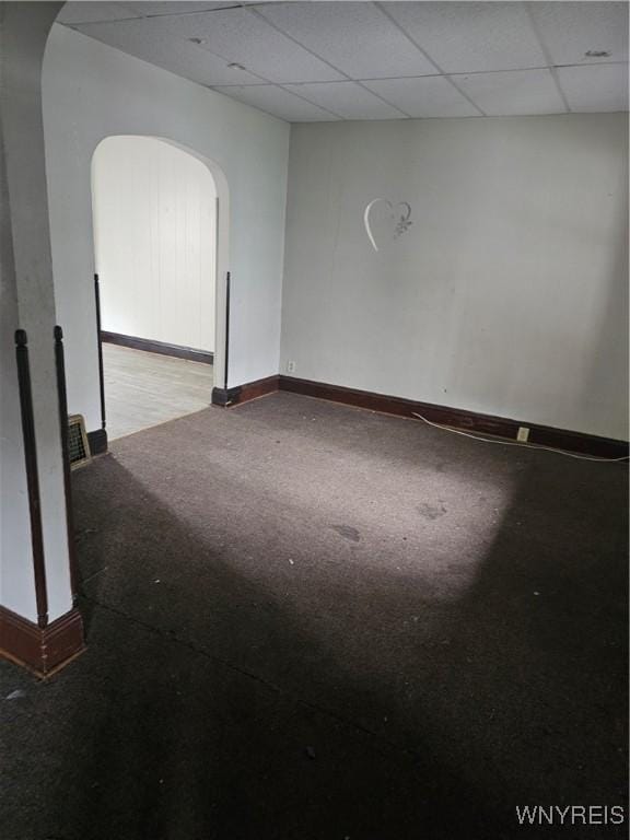 unfurnished room featuring arched walkways, a drop ceiling, light colored carpet, and baseboards