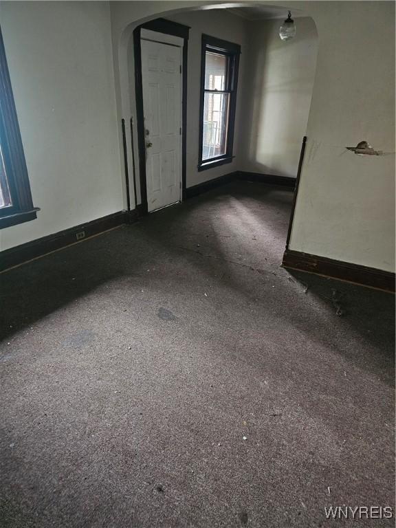 unfurnished room with carpet floors, baseboards, and arched walkways