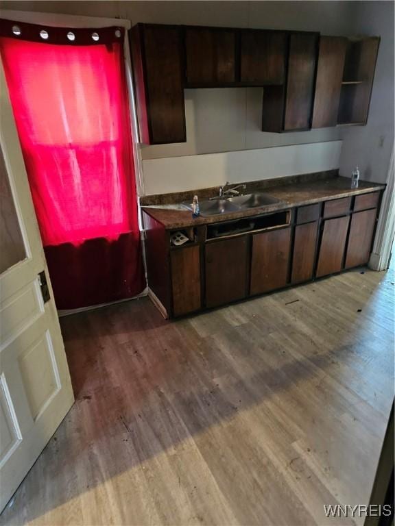 kitchen featuring dark countertops, wood finished floors, dark brown cabinetry, and a sink