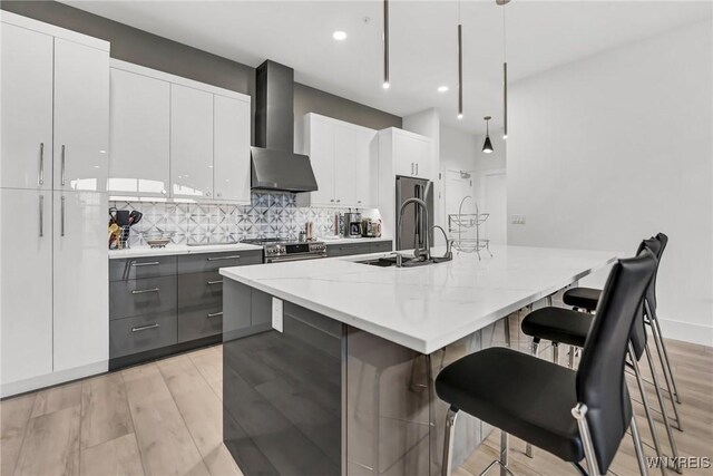 kitchen featuring pendant lighting, white cabinetry, gray cabinetry, a center island with sink, and wall chimney exhaust hood