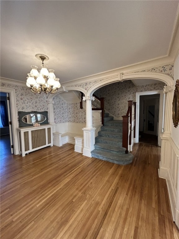 unfurnished living room featuring an inviting chandelier, ornamental molding, and wood-type flooring