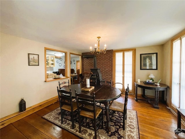 dining space with a chandelier, wood-type flooring, a healthy amount of sunlight, and a wood stove