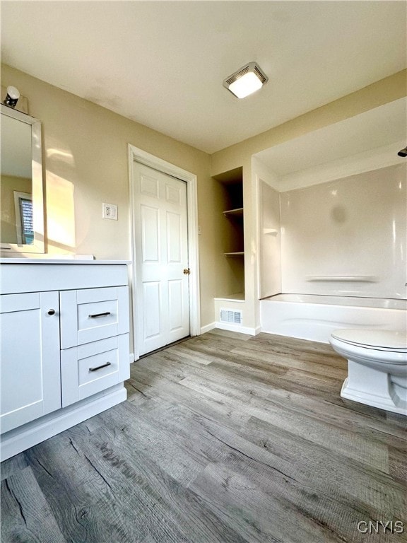 full bathroom with hardwood / wood-style flooring, toilet, built in features, vanity, and washtub / shower combination