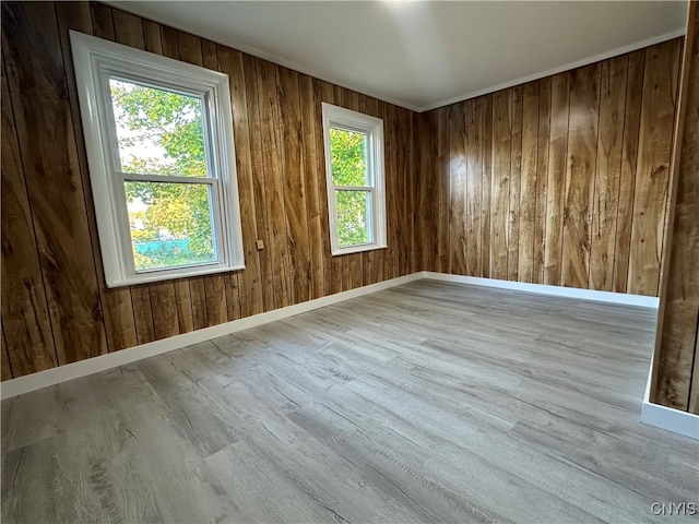 empty room with a wealth of natural light, light wood-type flooring, and wood walls