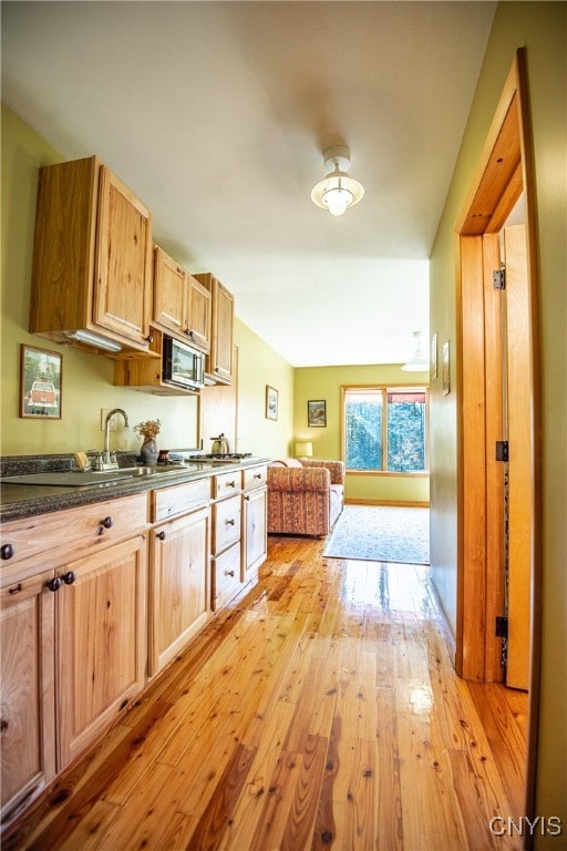 kitchen featuring stainless steel microwave, sink, light wood-type flooring, and light brown cabinets